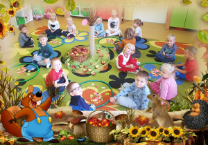 Grupa uśmiechniętych dzieci siedzi na dywanie, na którym znajdują się dekoracje z jabłek.